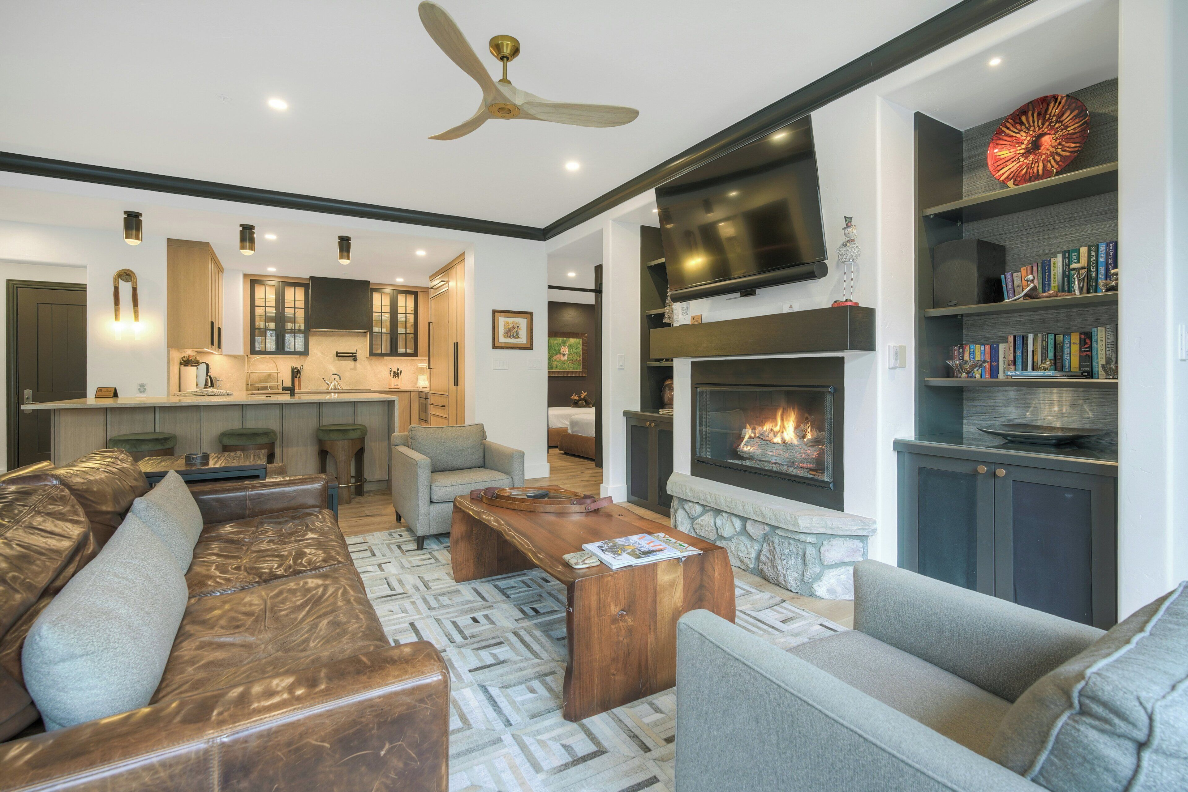 A modern living room with a fireplace, leather sofas, a wooden coffee table, and a bookshelf.