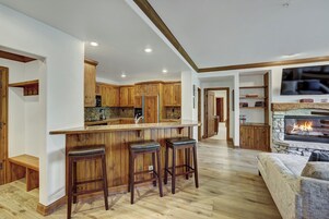 Una cocina moderna con armarios de madera, una isla central con taburetes de bar y una chimenea de piedra.