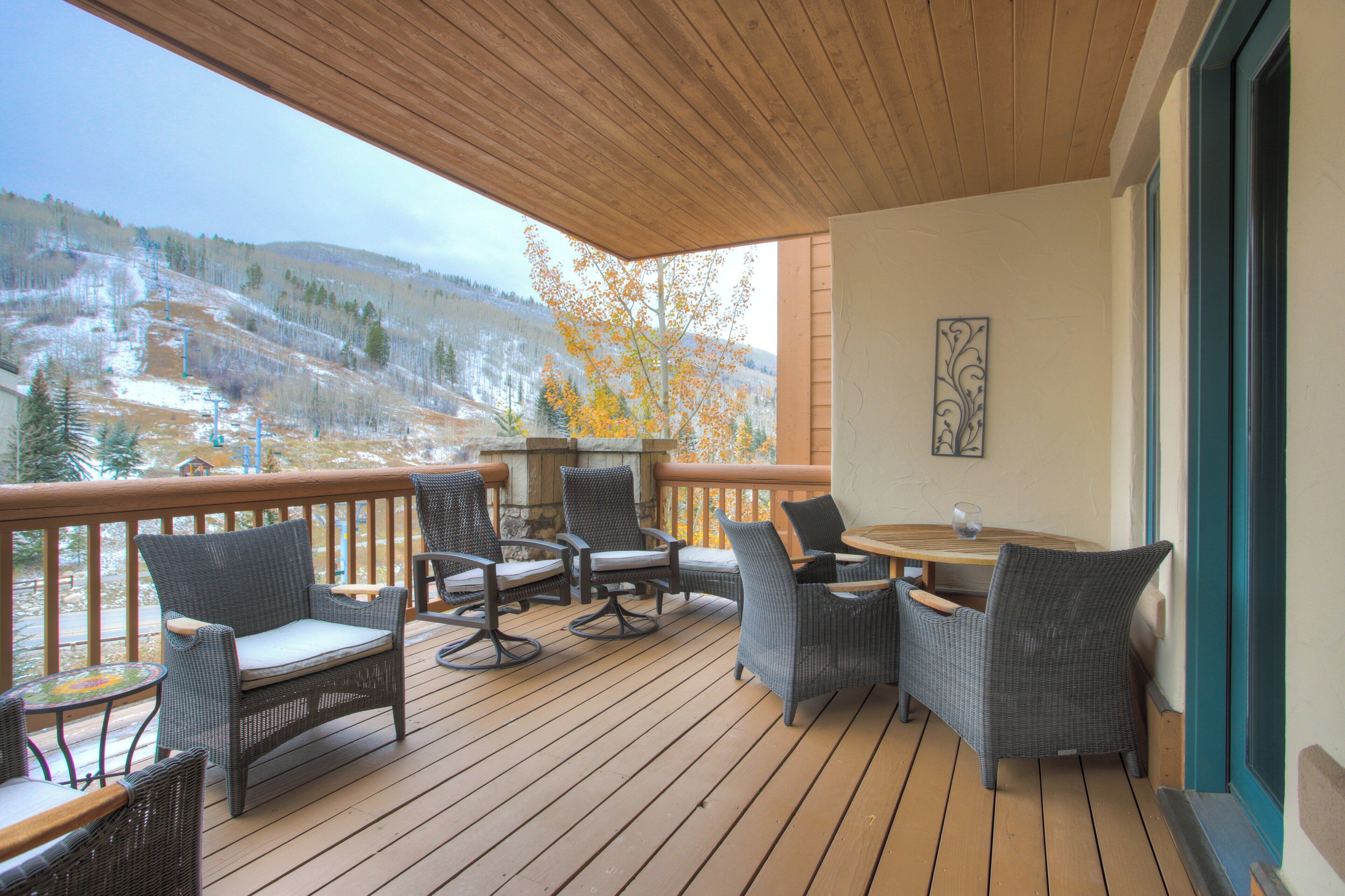 A wooden deck with wicker furniture and a table, overlooking a snowy landscape.