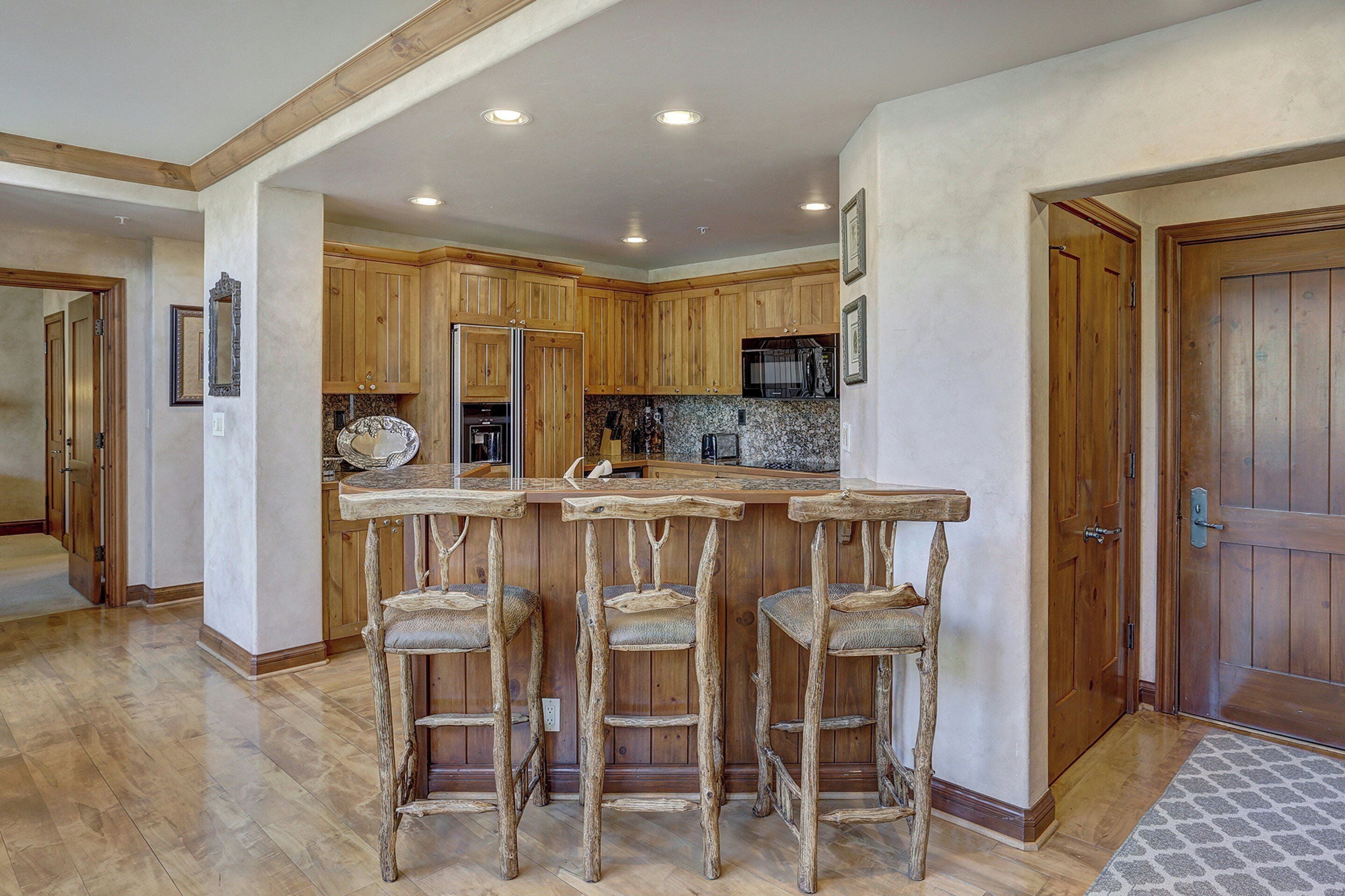 Cocina con armarios de madera, encimera de granito y una barra con tres taburetes.