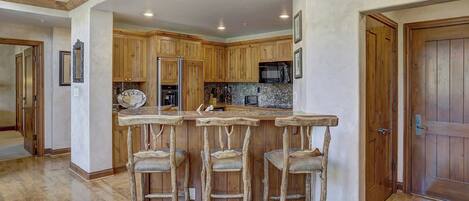 Cocina con armarios de madera, encimera de granito y una barra con tres taburetes.