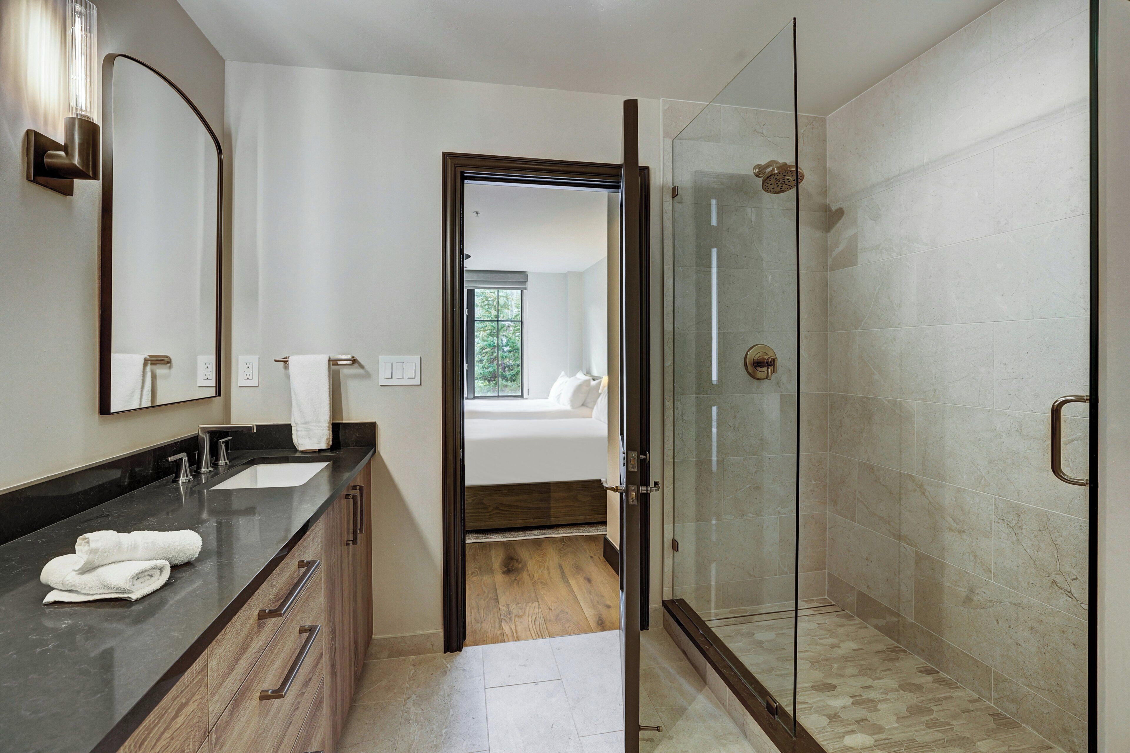 Une salle de bain moderne avec une douche à parois de verre, un meuble-lavabo doté d’un plan de travail foncé et un grand miroir.