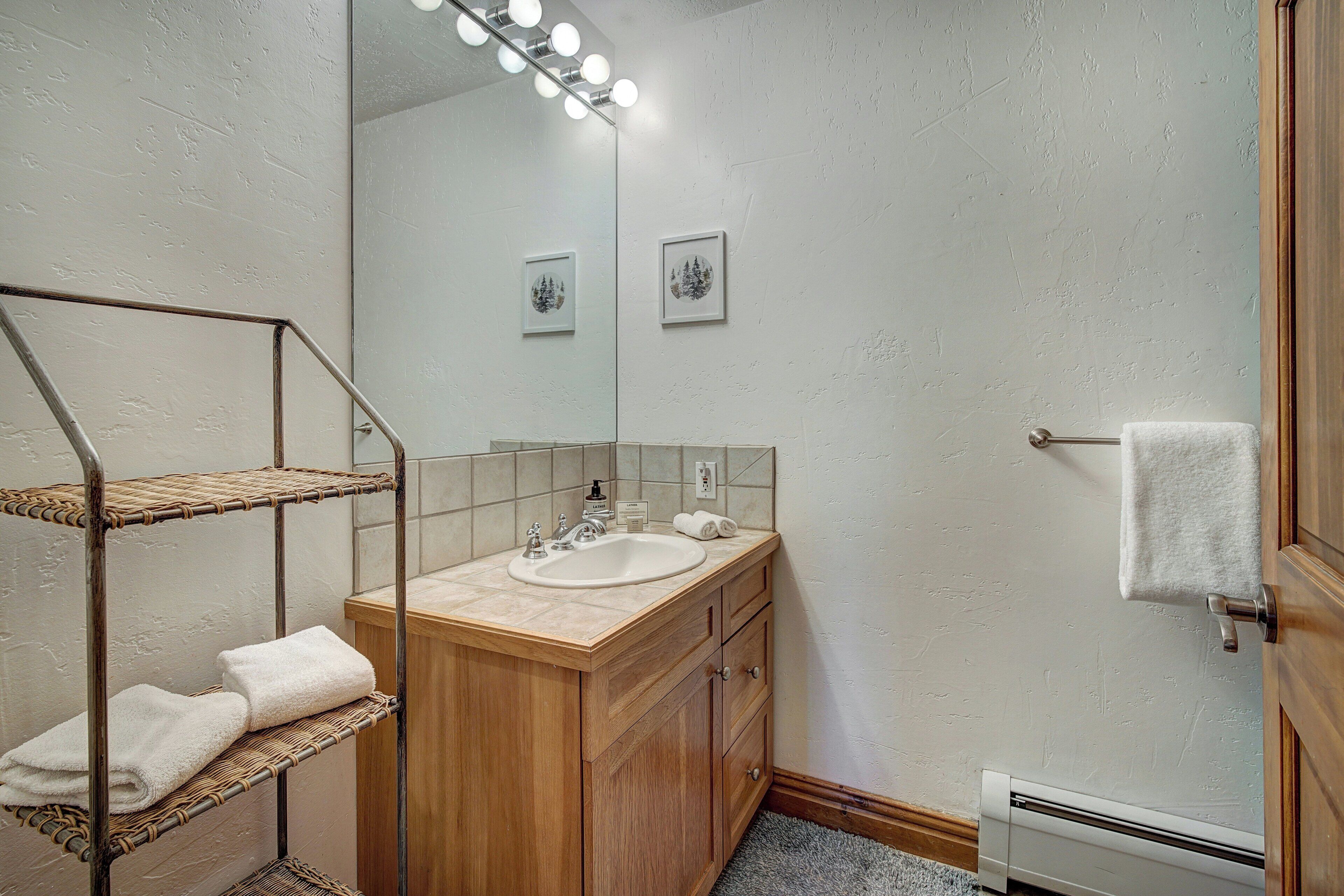 Un bagno con mobiletto in legno, lavabo, specchio con illuminazione e portasci.