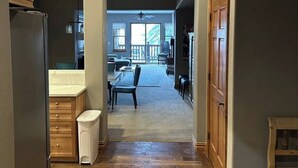 A hallway with wooden flooring, a kitchen area with a refrigerator, and a dining area with a table and chairs. - Lodge at Brookside, A Vail Resorts Property (Avon)