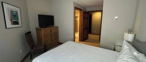 A hotel room with a bed, a television on a dresser, a chair, and a door leading to another room.