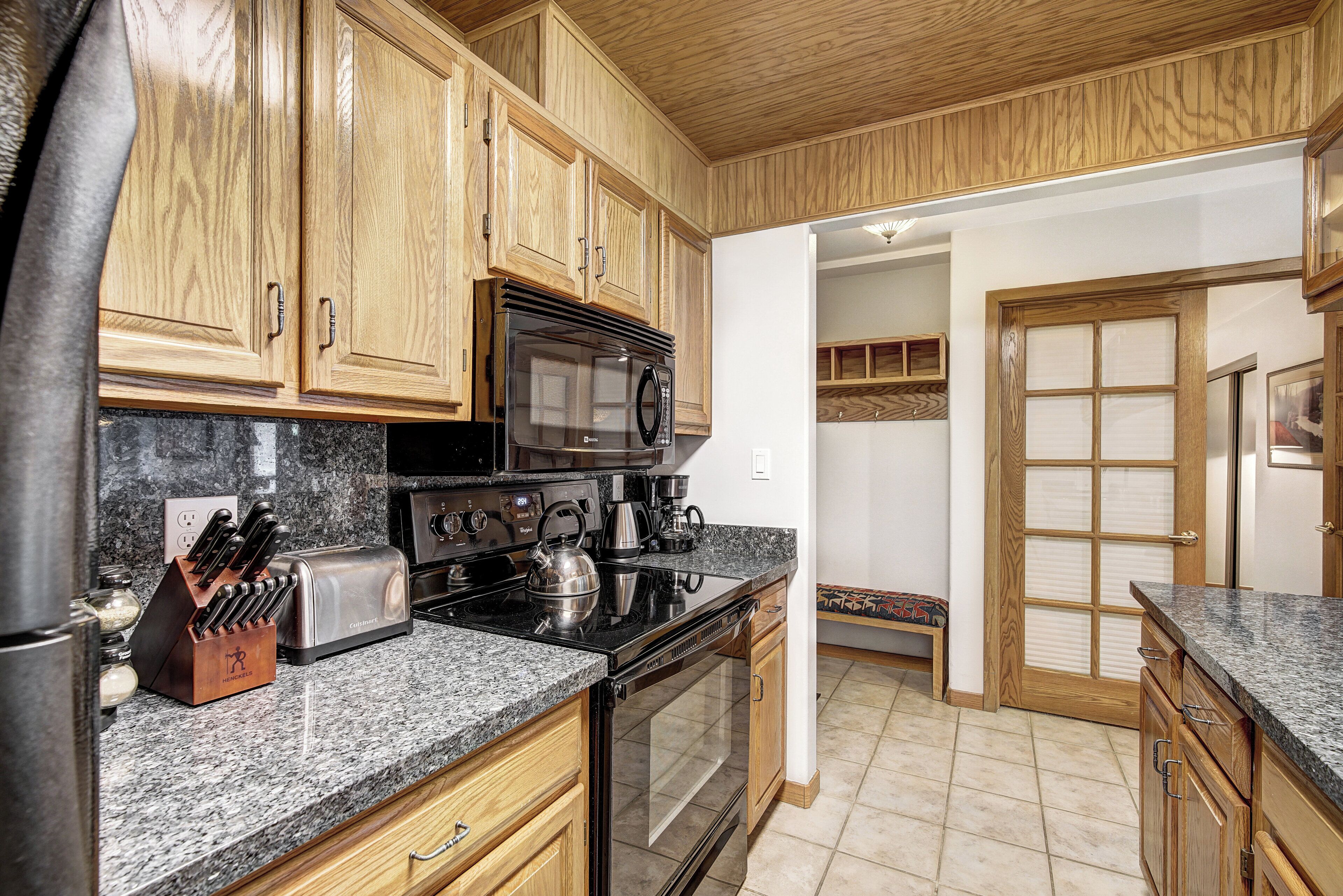 A kitchen with wooden cabinets, a stainless steel refrigerator, a microwave, a toaster, and a knife block.