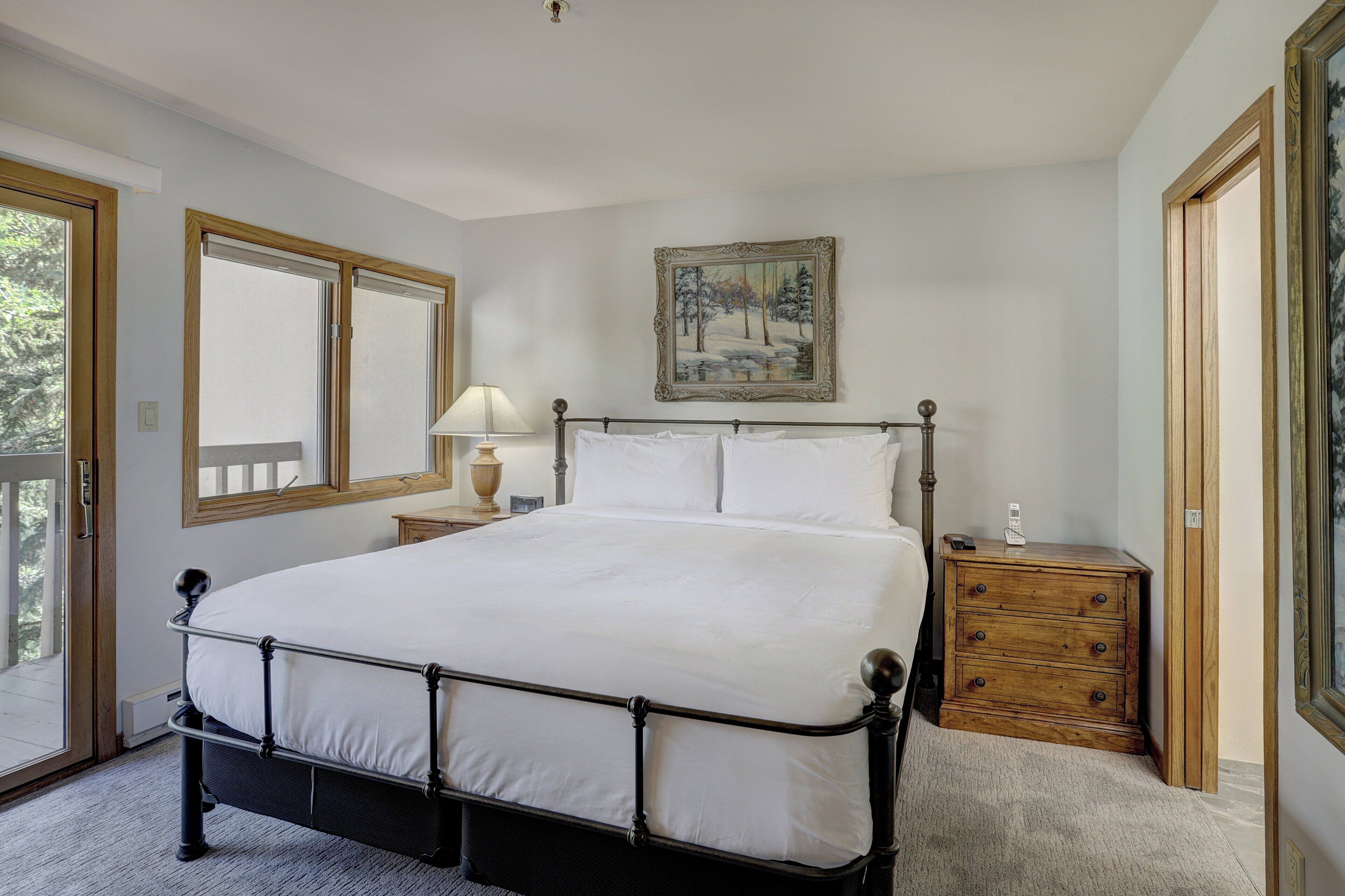 A bedroom with a large bed, a nightstand with a lamp, a dresser, and a painting on the wall.