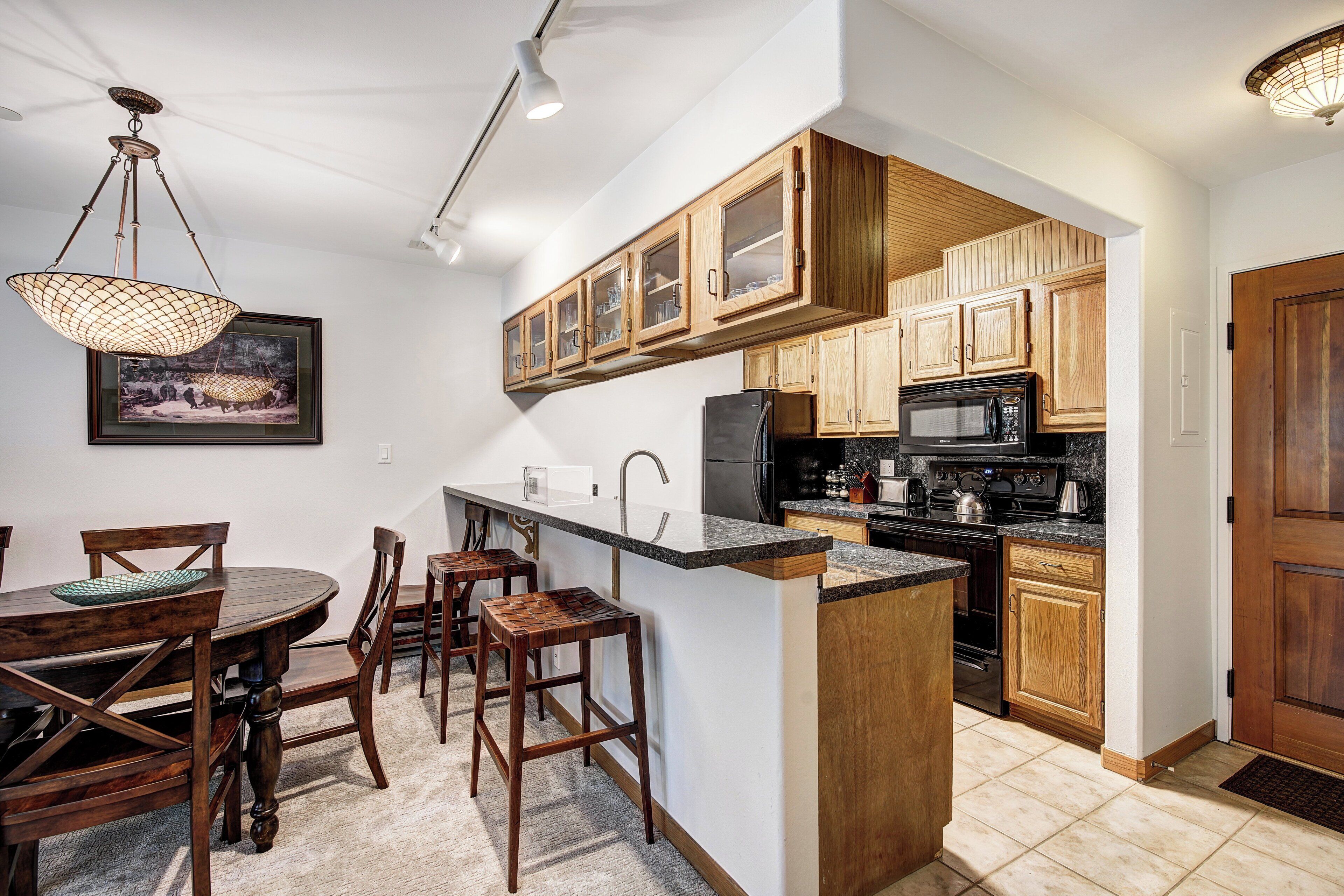 A kitchen with wooden cabinets, a refrigerator, a microwave, and a dining area with a table and chairs.