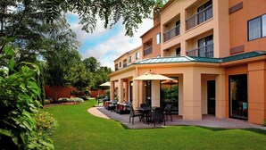 A hotel with a covered outdoor seating area, a well-maintained lawn, and a multi-story building with balconies. - Courtyard by Marriott Newark Granville (Newark)