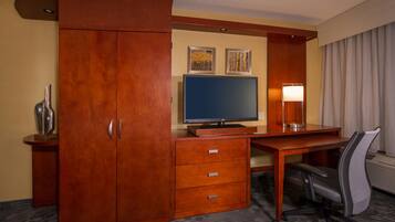 A hotel room with a wooden desk, a flat-screen TV, a lamp, and a chair.