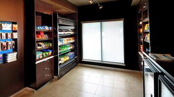 A clean, well-lit snack bar with shelves stocked with various beverages and snacks, a large window providing natural light, and a tiled floor.