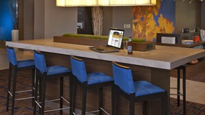 A modern hotel lobby with a long reception desk, blue upholstered bar stools, a laptop, and a bottle of Moon beer. - Courtyard by Marriott Newark Granville (Newark)