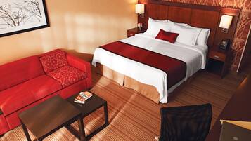 A hotel room with a bed, a red sofa, a small table, and a chair.