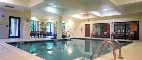 Una piscina interior con agua cristalina, una silla de socorrista y una escalera de piscina.