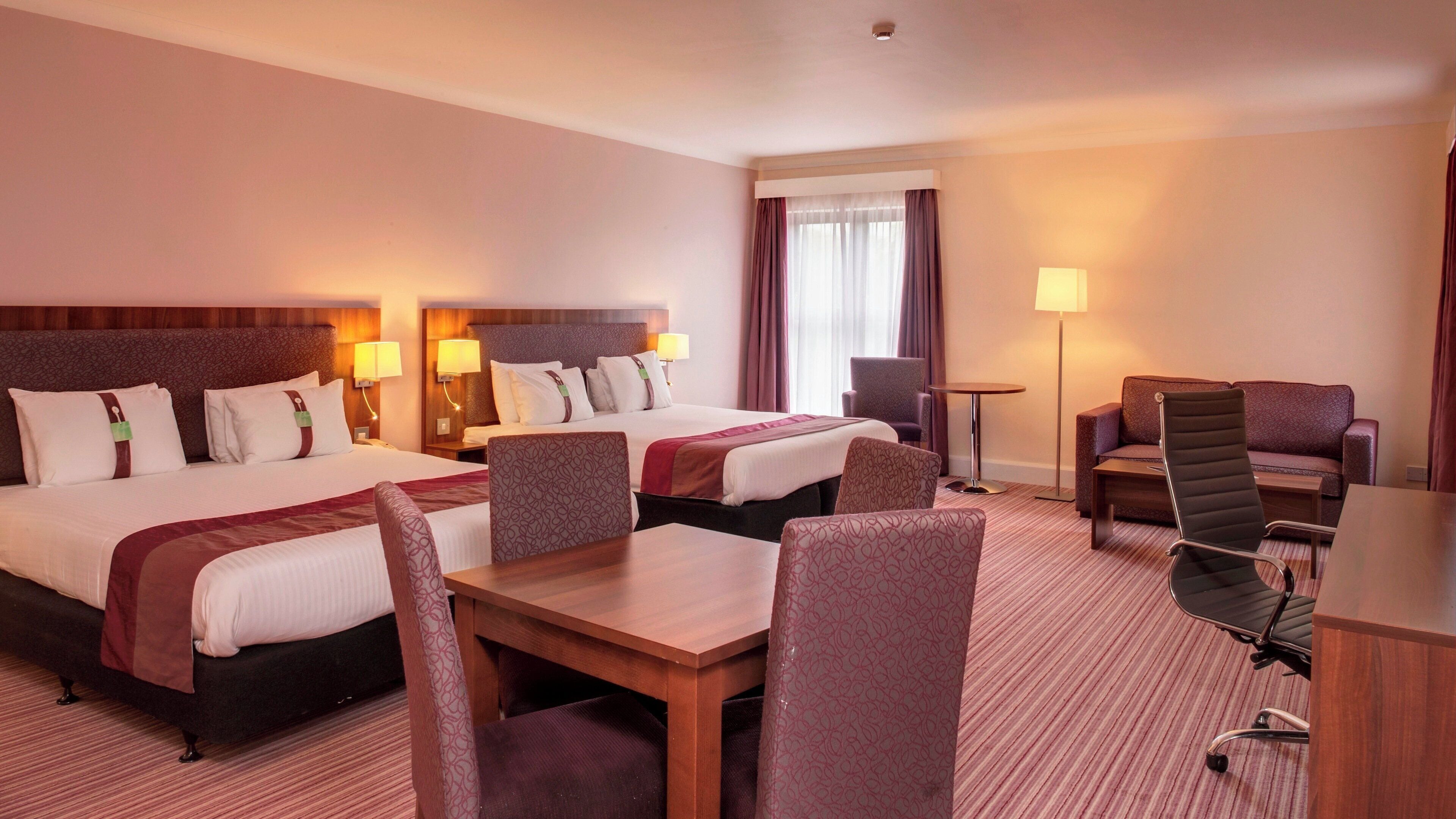 A hotel room with two beds, a desk, a chair, and a sofa.