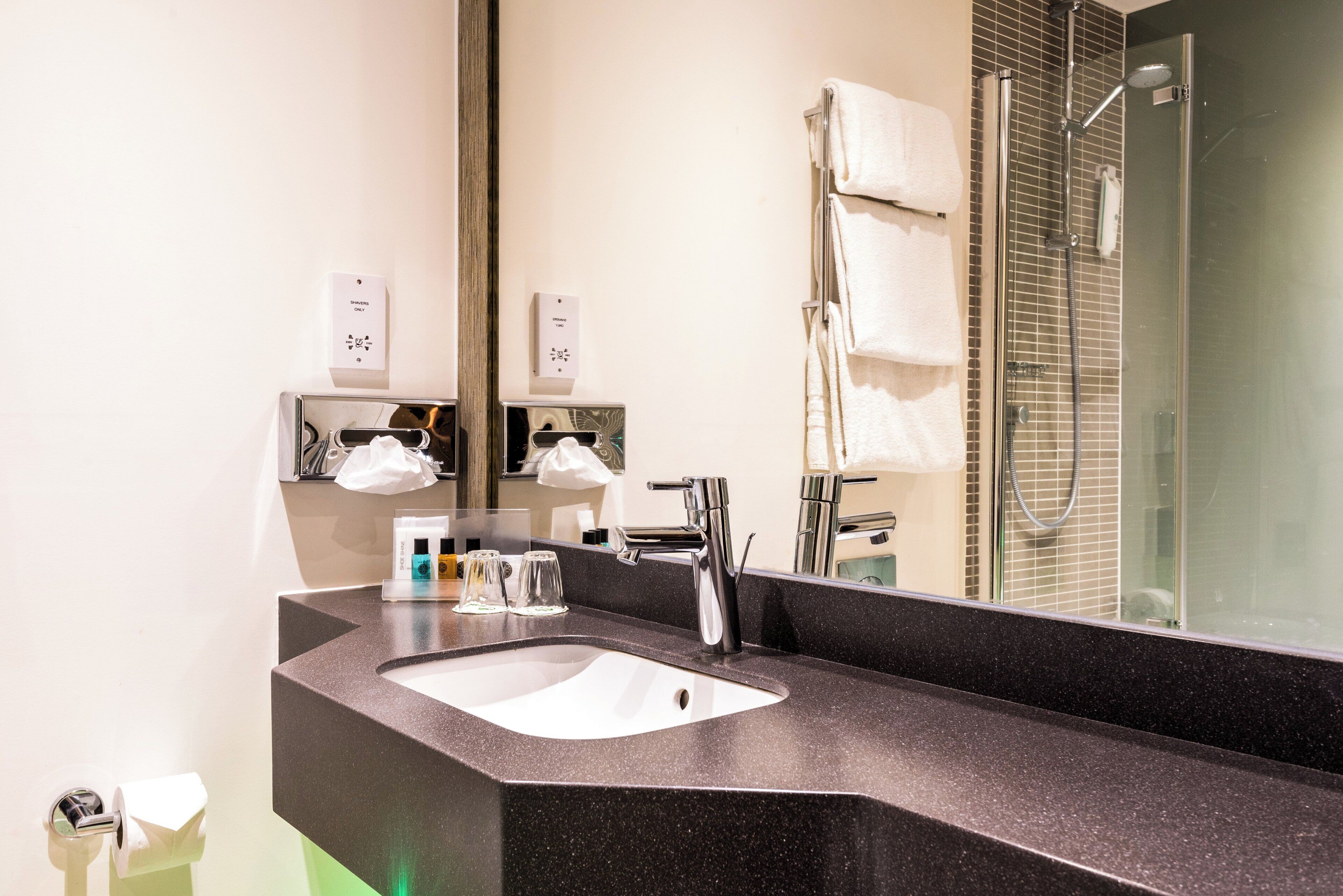 Un baño moderno con encimera negra, lavabo, espejo y zona de ducha.
