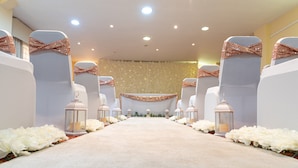 A carpeted aisle with white chairs and lanterns, leading to a stage with a floral backdrop. - Holiday Inn Rotherham Sheffield by IHG (Rotherham)