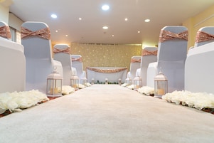 A carpeted aisle with white chairs and lanterns, leading to a stage with a floral backdrop.