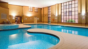 An indoor swimming pool with tiled walls, a clock, and a lifeguard chair.