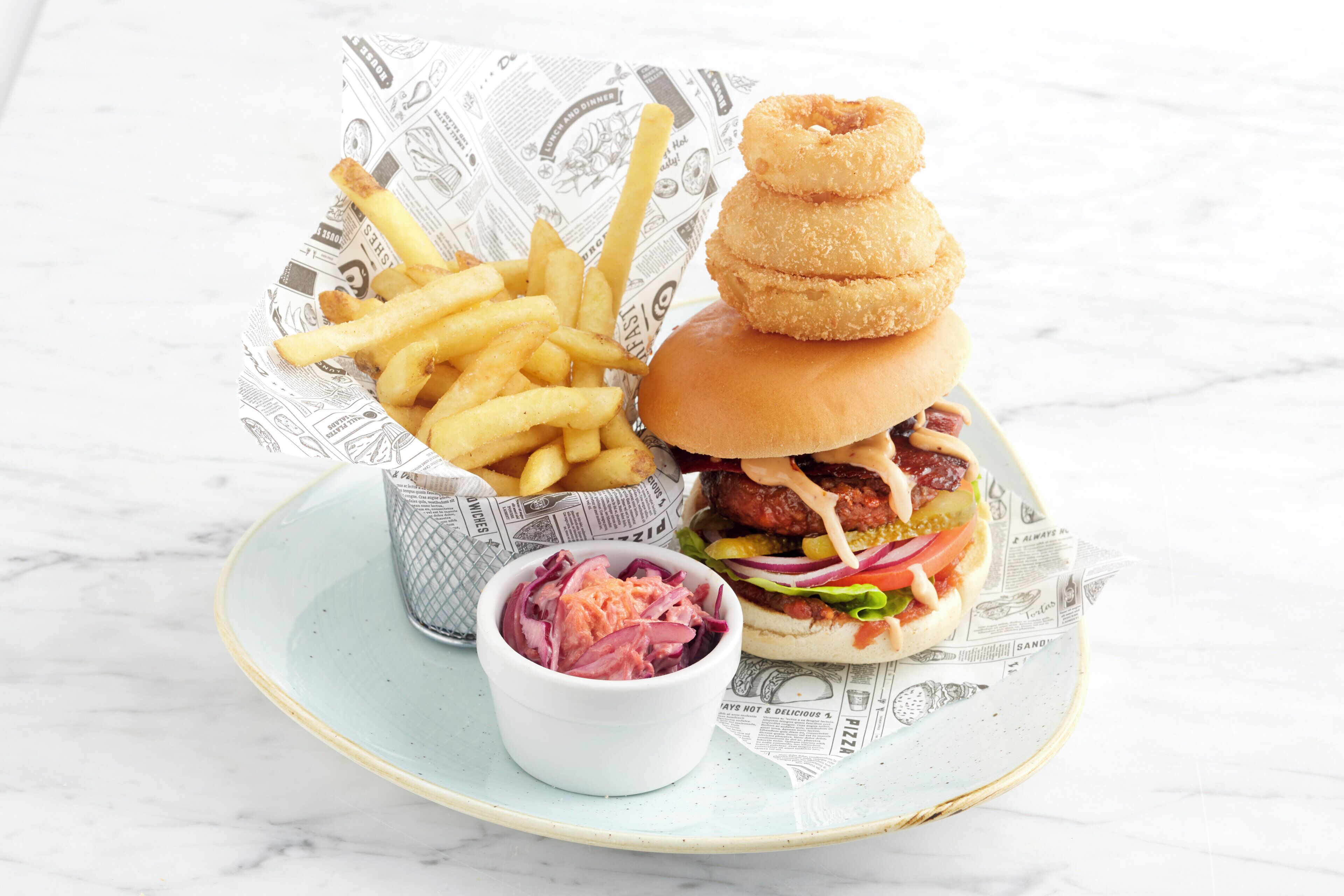 Un plato con una hamburguesa, papas fritas, aros de cebolla y un pequeño bol de ensalada de col.