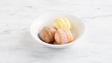 A white bowl containing three scoops of ice cream on a marble surface.