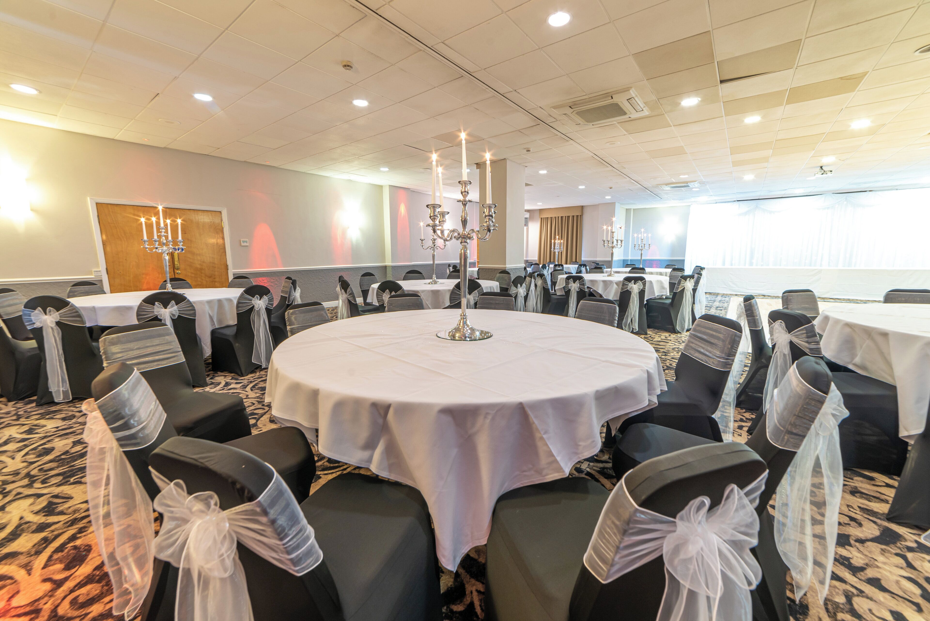 A conference room with round tables, black chairs with white sashes, and a chandelier.
