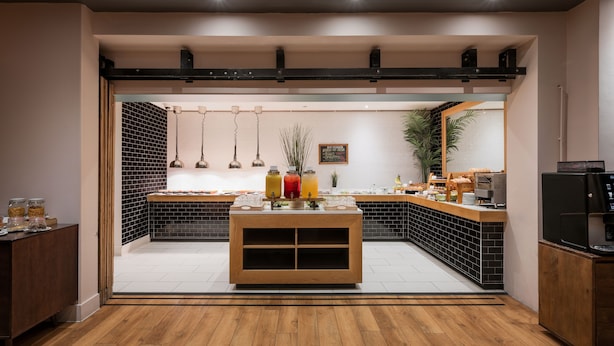 A breakfast bar with a variety of food items and beverages, a coffee machine, and a plant. - Holiday Inn Rotherham Sheffield by IHG (Rotherham)