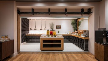 A breakfast bar with a variety of food items and beverages, a coffee machine, and a plant.