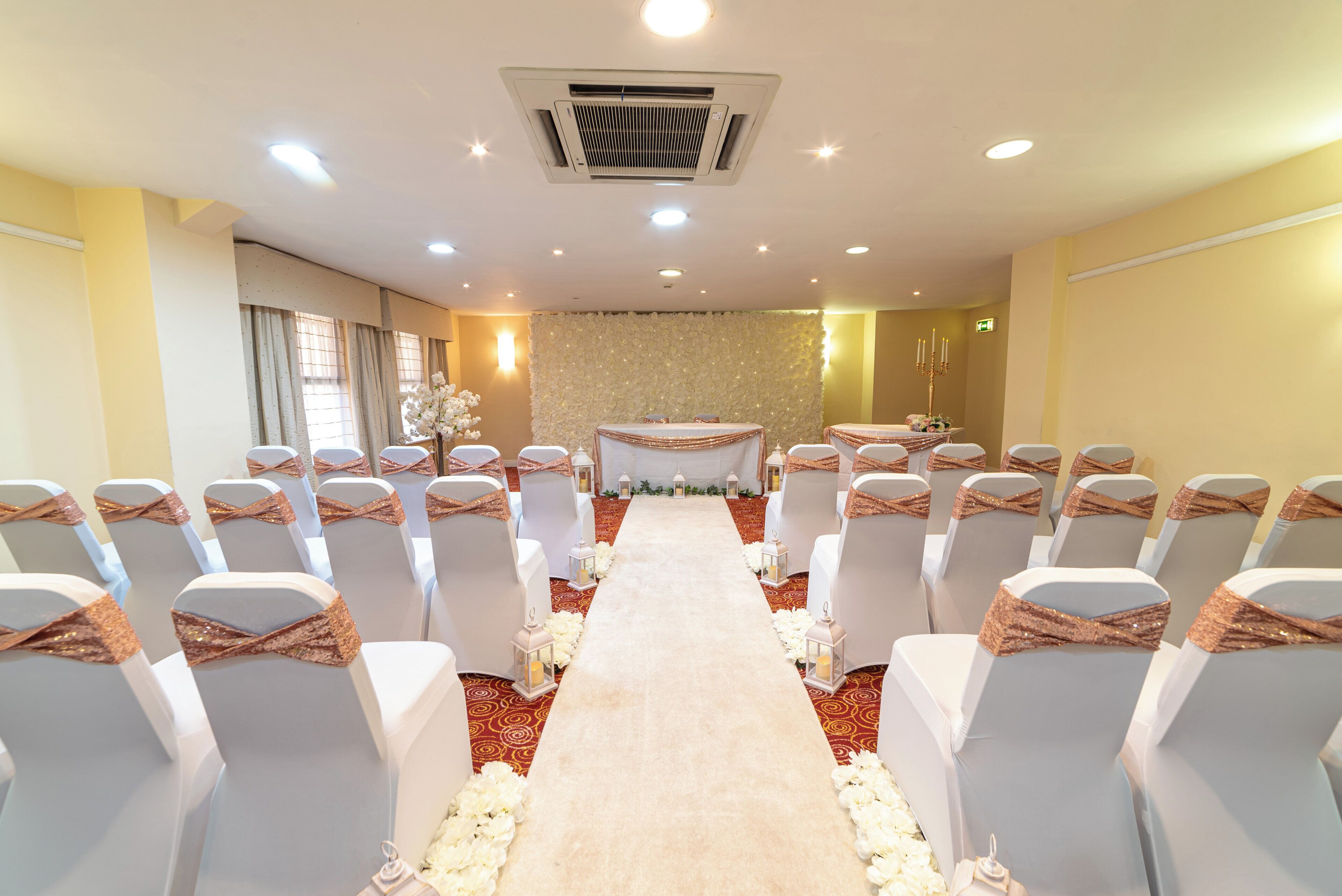 Une cérémonie de mariage avec des rangées de chaises, une allée recouverte de tapis, des décorations florales et un mur orné de fleurs.