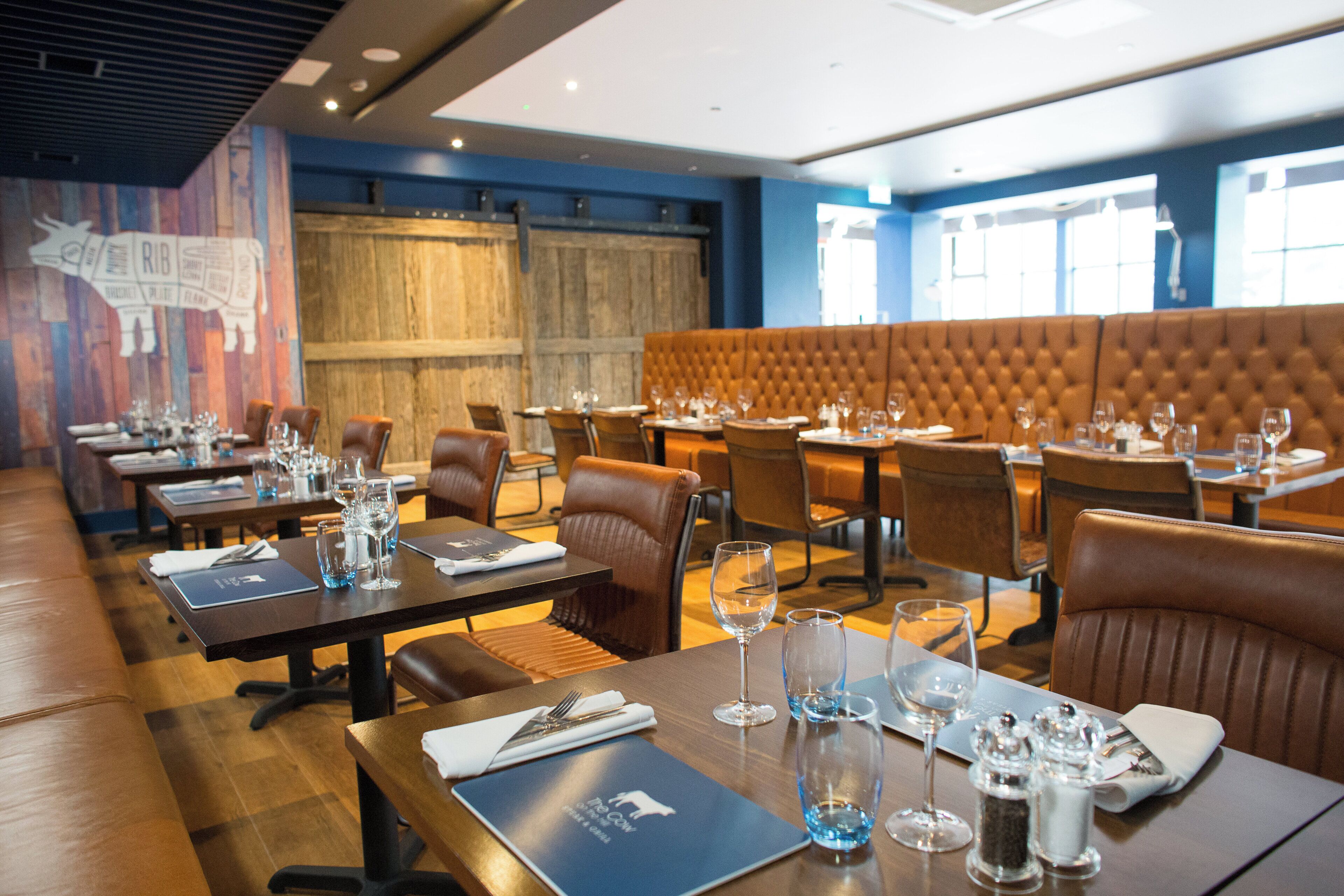 A restaurant with multiple tables, each set with cutlery, glasses, and menus.