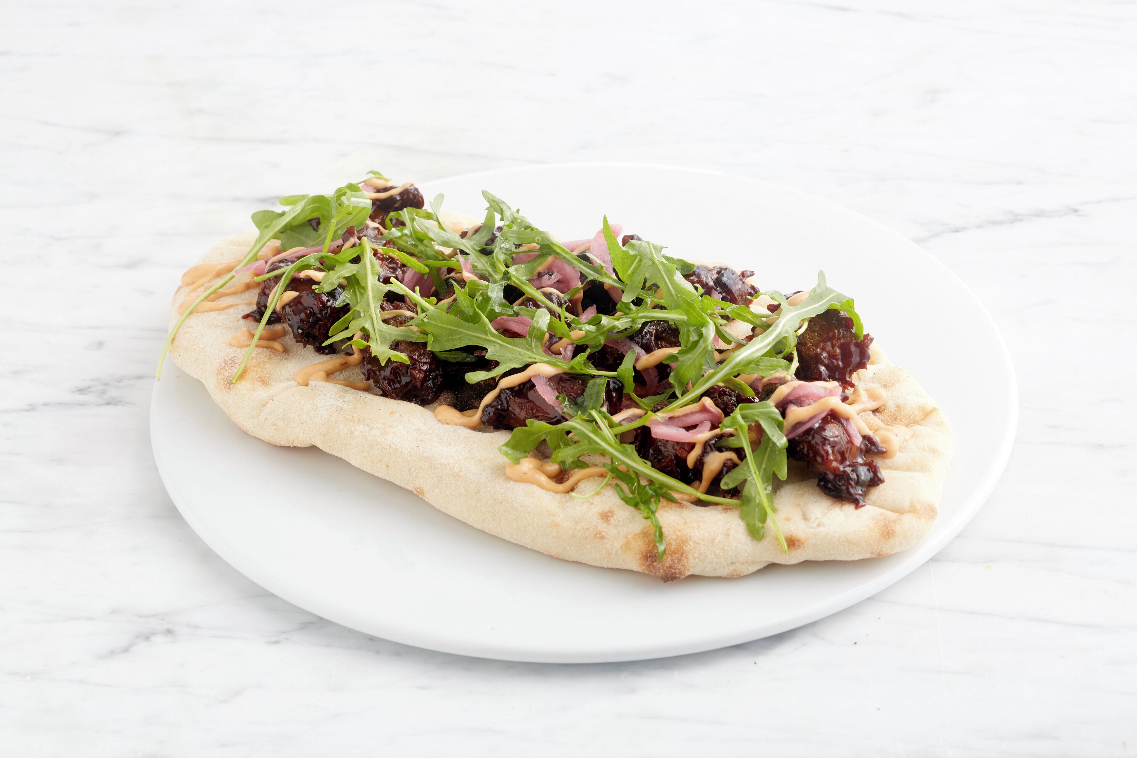 Une galette garnie de légumes verts et de viande, servie sur une assiette blanche.