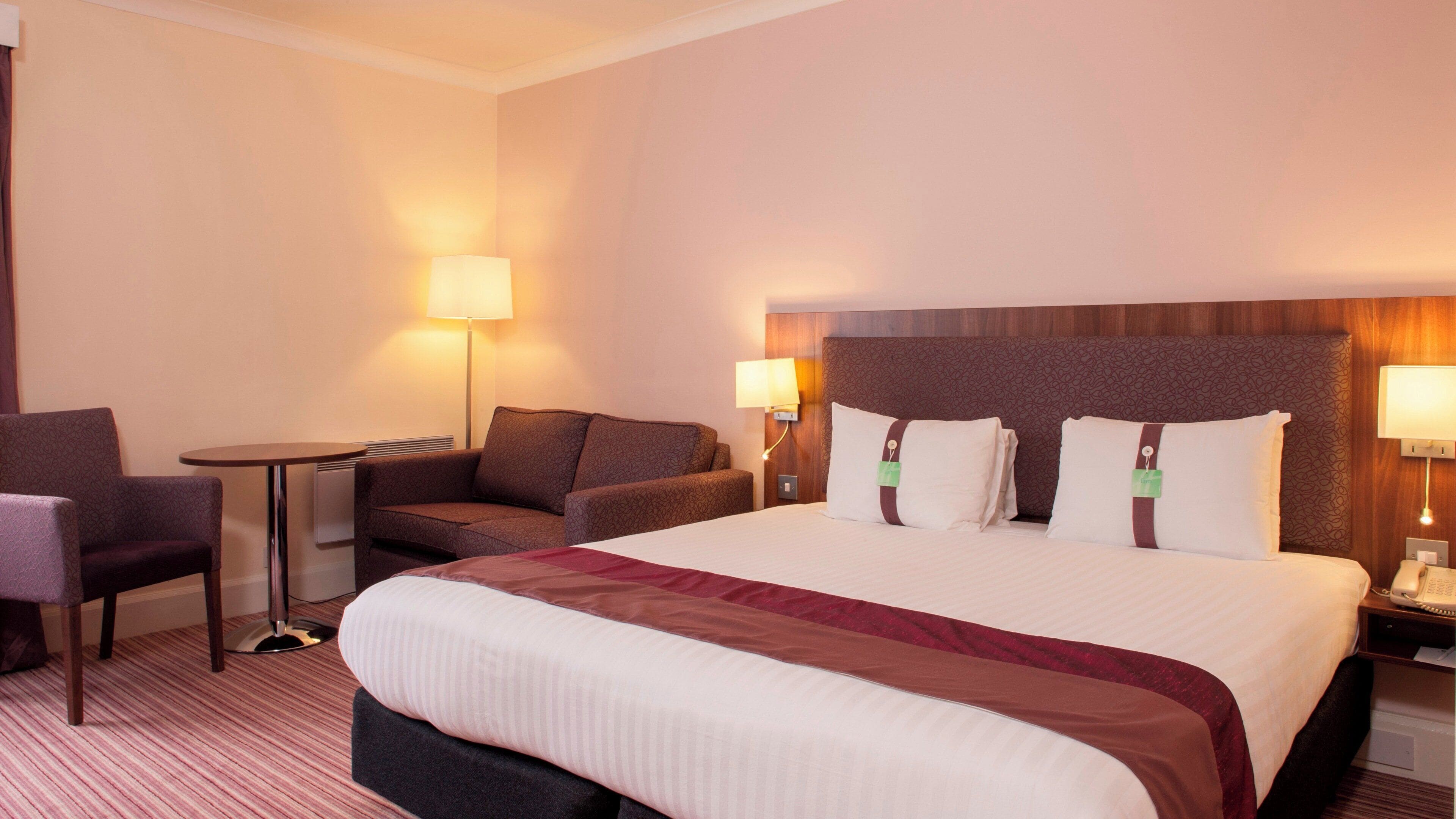 A hotel room with a large bed, two bedside tables, a chair, and a small table.