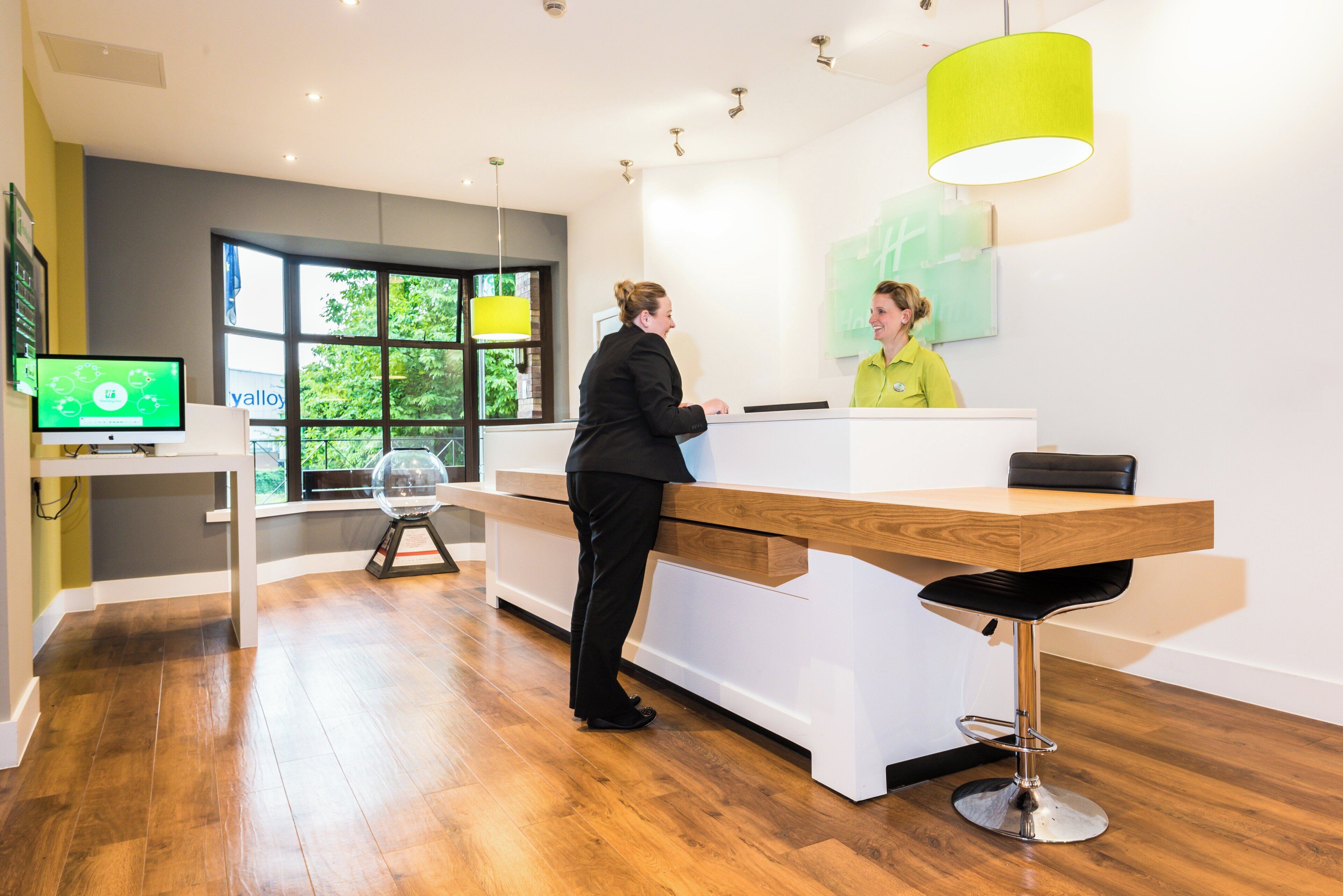 A reception desk with a modern design, a digital screen, and a window providing a view of greenery outside.