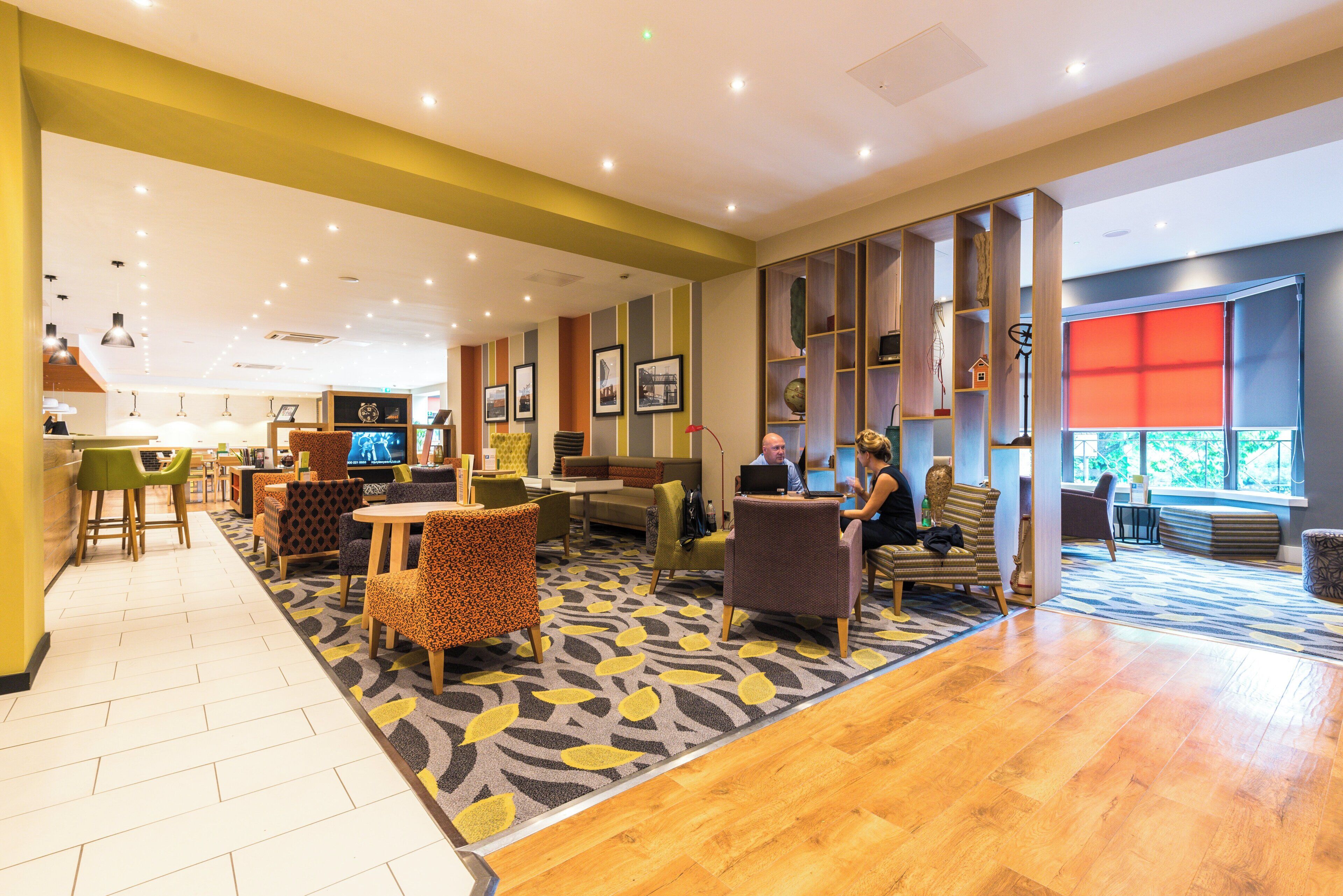 A hotel lobby with seating areas, a reception desk, and a television screen.