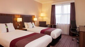Two beds with matching headboards and bedside lamps, a small table, and a desk with a chair.
