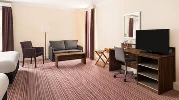 Una habitación de hotel con cama, sofá, escritorio con televisor, silla y lámpara.