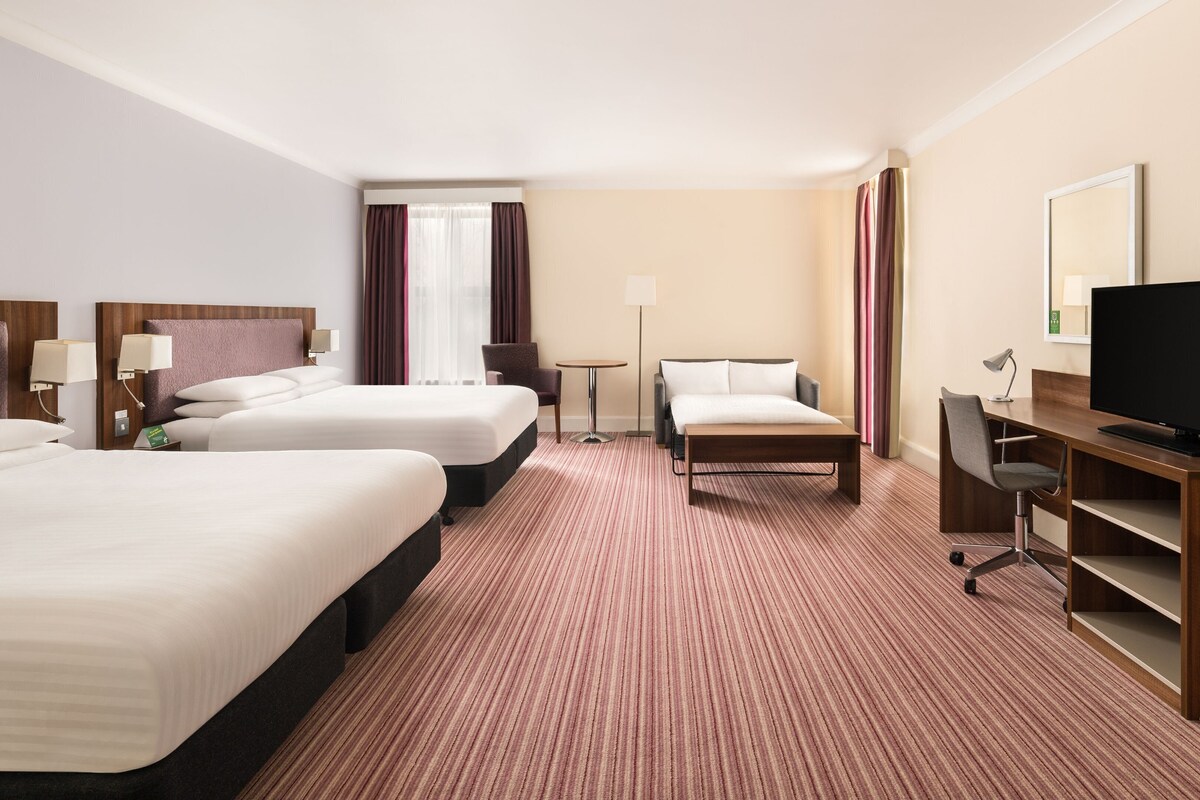 A hotel room with two beds, a desk with a TV, a chair, and a lamp.