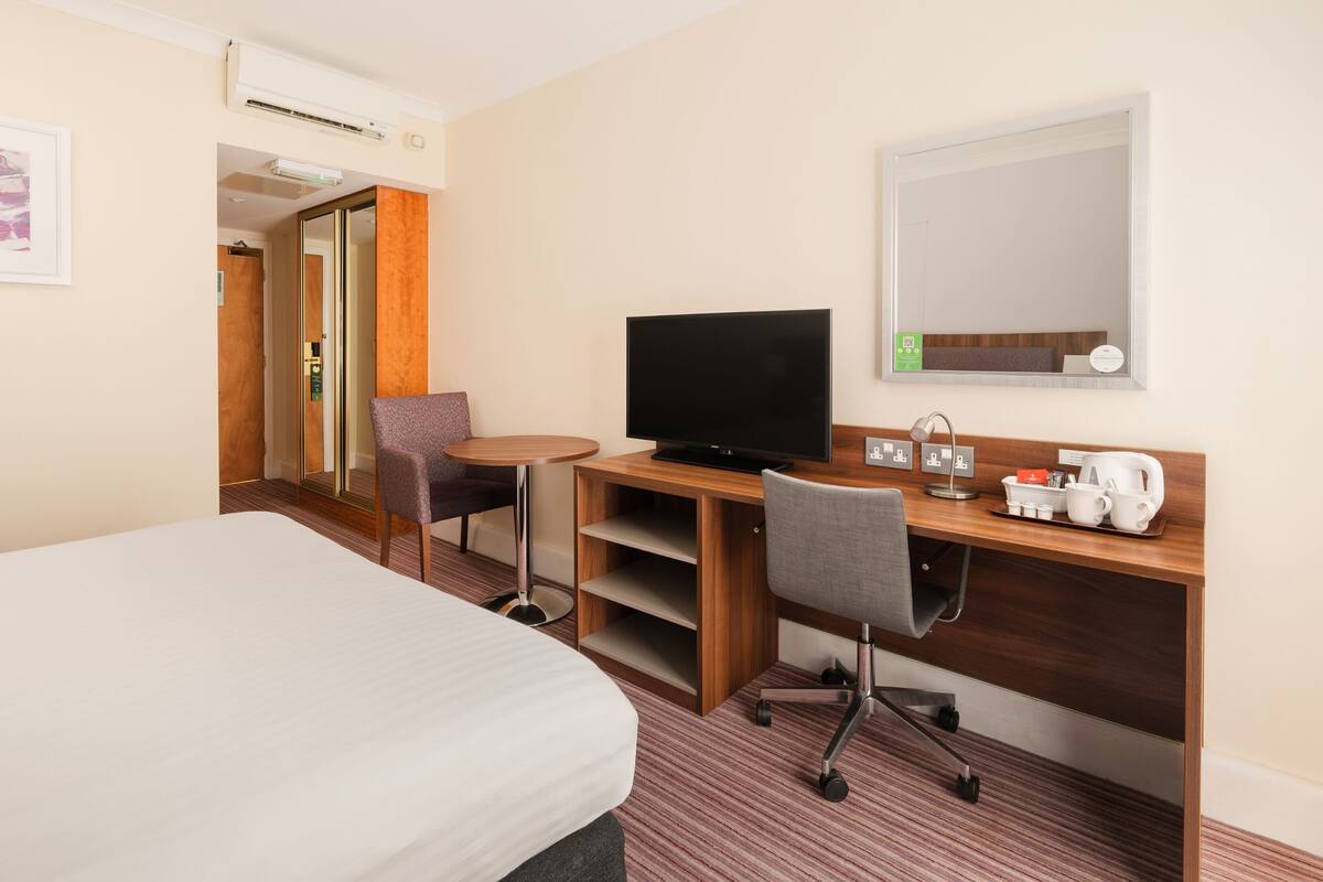 Une chambre d’hôtel comprenant un lit, un bureau avec une télévision, une chaise, une machine à café et un miroir.