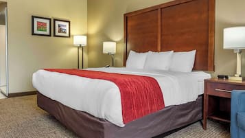 A hotel room with a large bed, a wooden headboard, two bedside lamps, and a small desk with a chair.