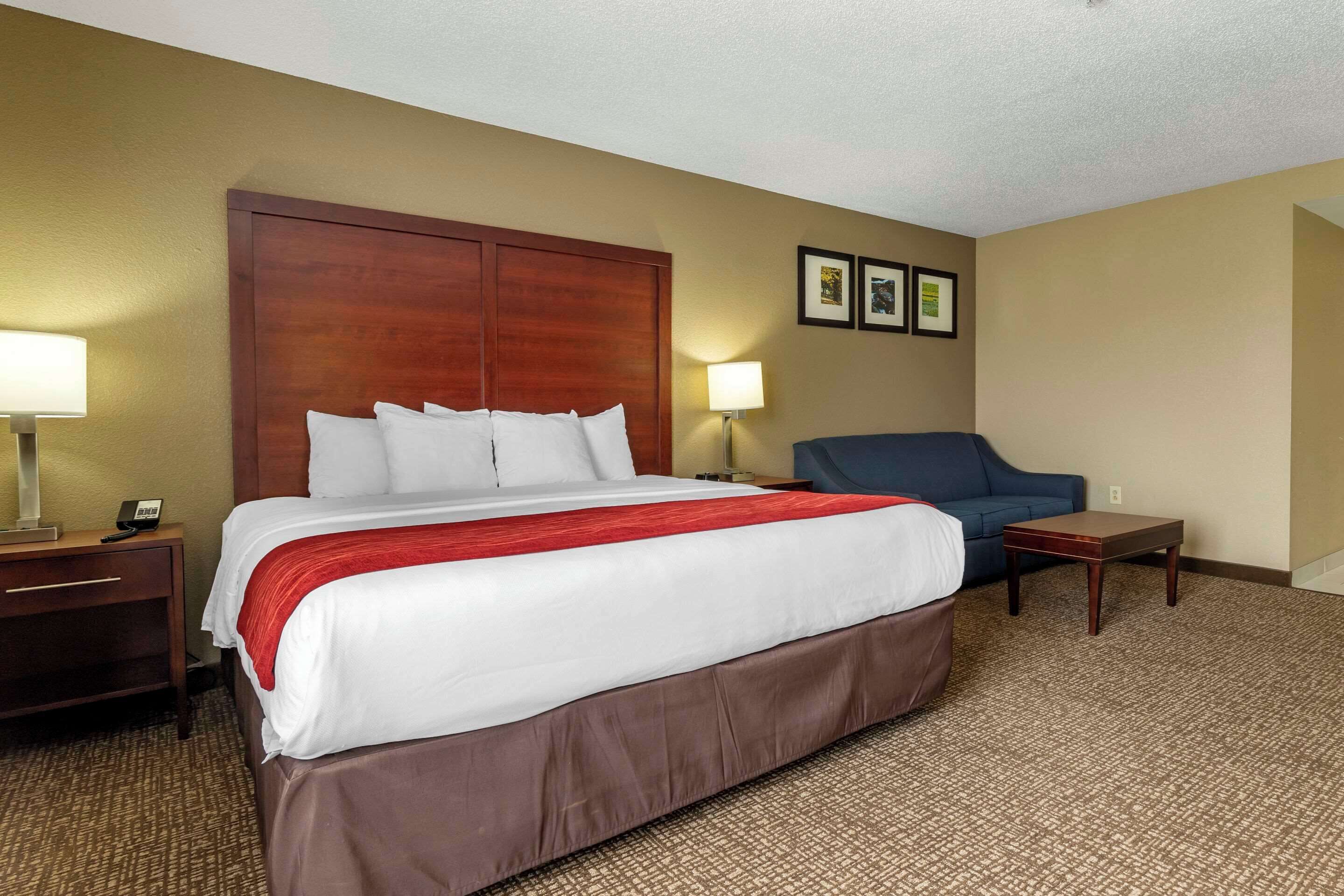 A hotel room with a large bed, a nightstand, a desk, a chair, and a small table.