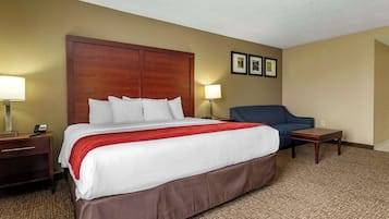 A hotel room with a large bed, a nightstand, a desk, a chair, and a small table.