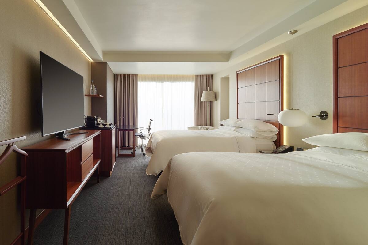 A hotel room with a TV, two beds, a desk, and a chair.