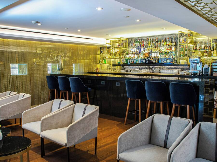 A bar area with multiple seating options, a bar counter with a variety of bottles, and a patterned wall.