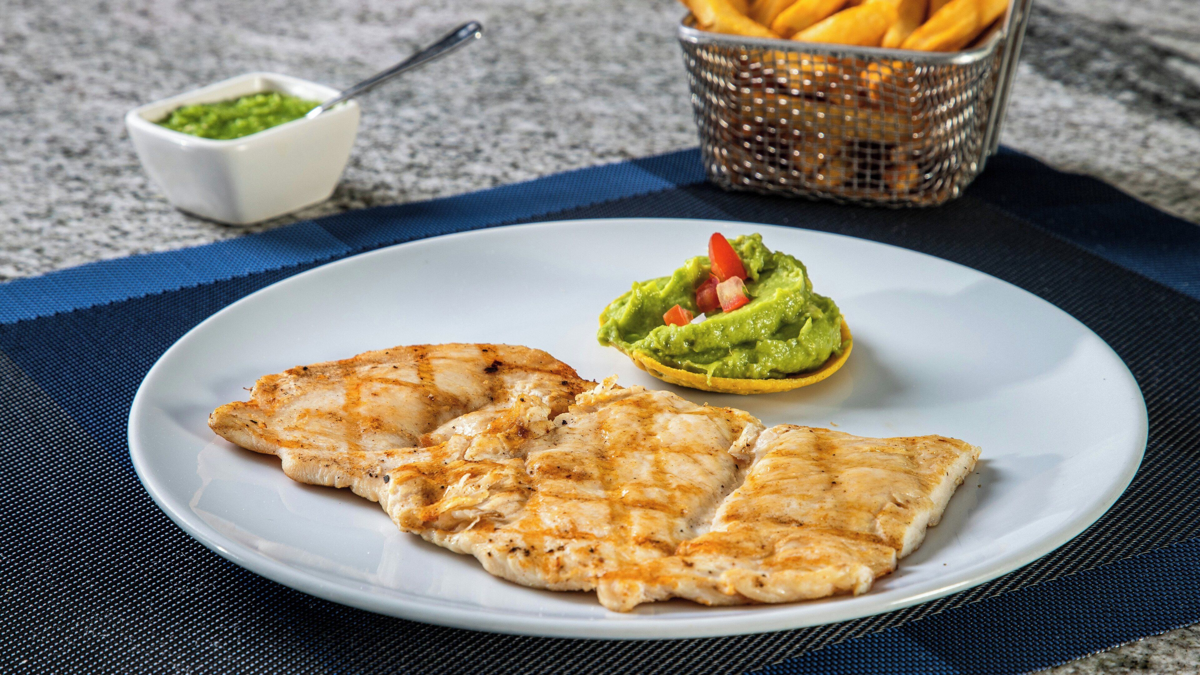 Un plato con pollo a la parrilla y guacamole sobre un tapete azul.