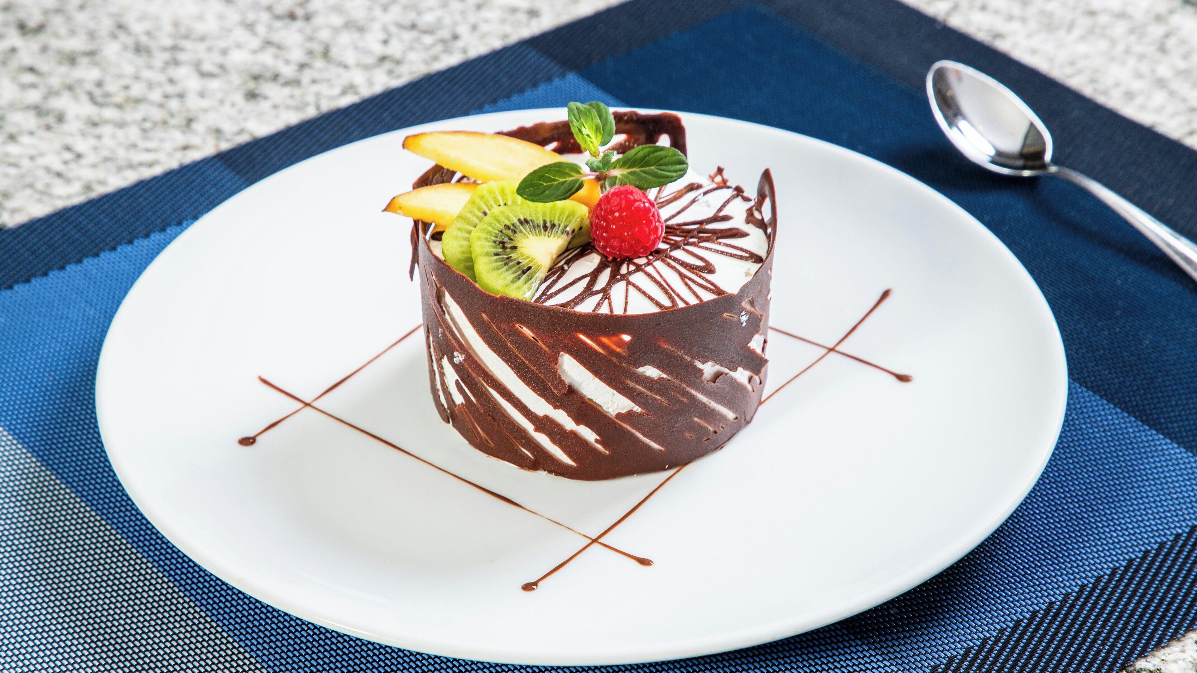 A dessert on a white plate with chocolate and fruit toppings, placed on a blue placemat.