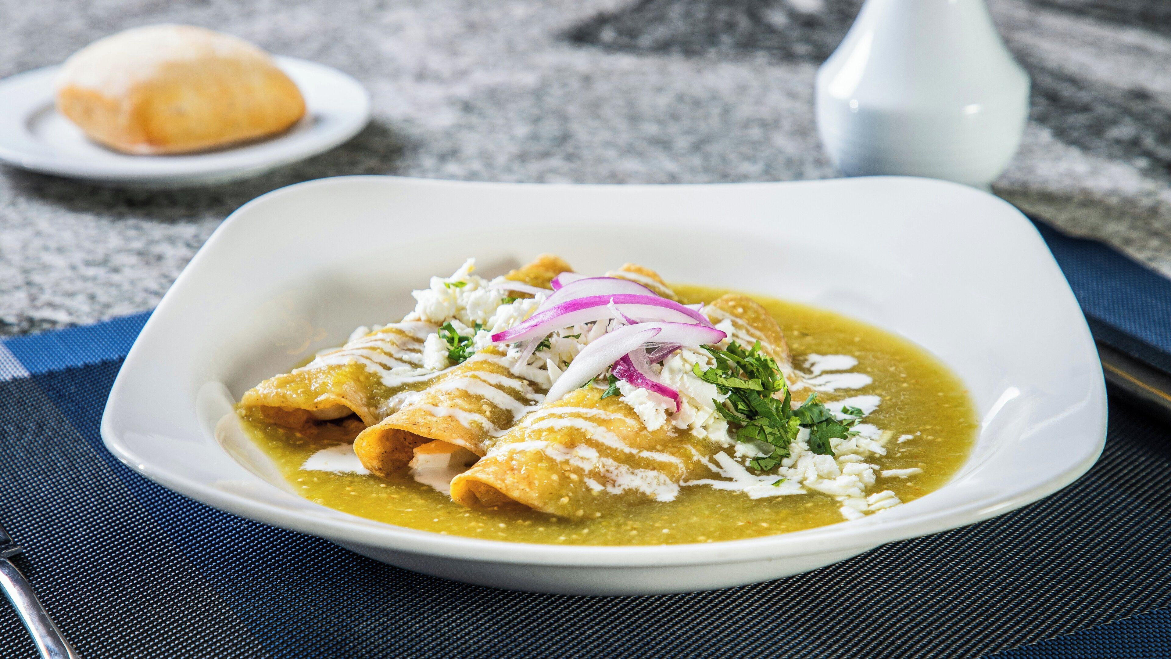 Ein Teller Enchiladas mit grüner Sauce, belegt mit Zwiebeln und Käse.