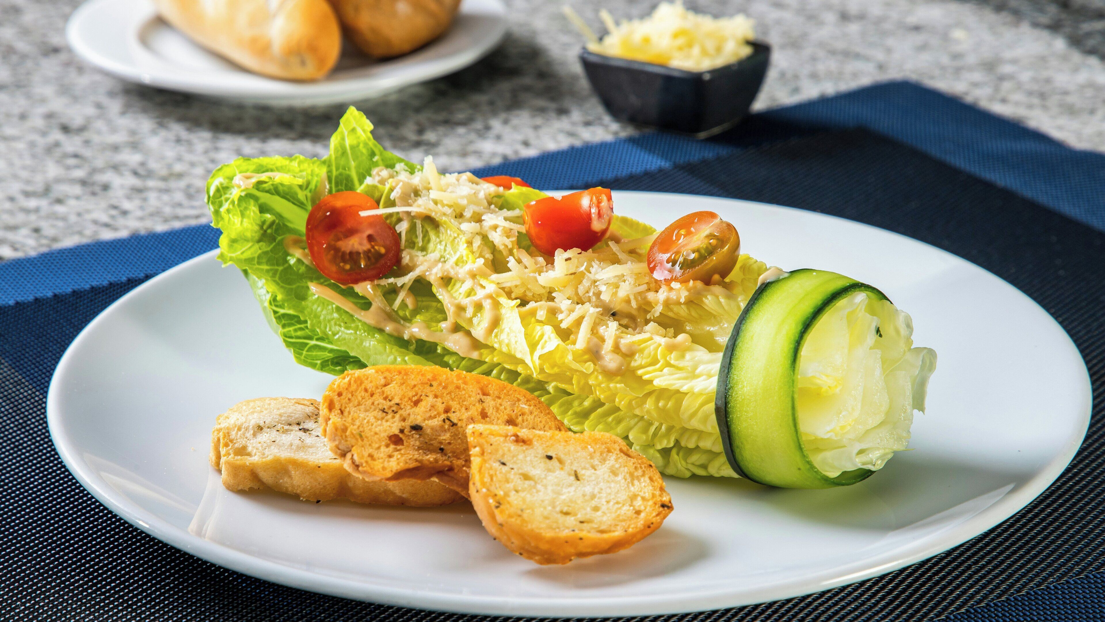 Um prato com salada, uma fatia de pepino e duas fatias de pão sobre uma mesa.