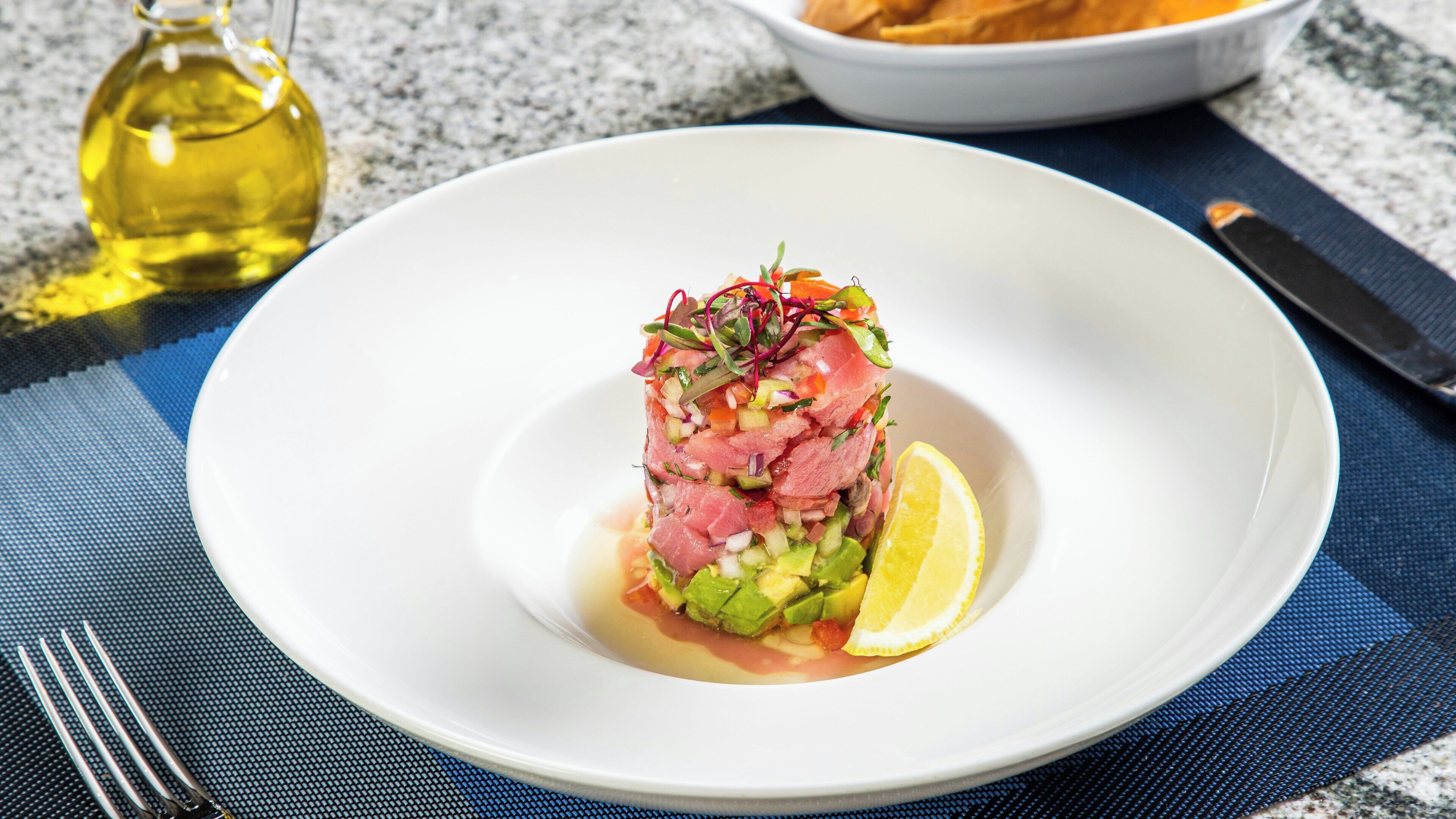 A white plate with a layered dish, a lemon half, and a bottle of oil in the background.
