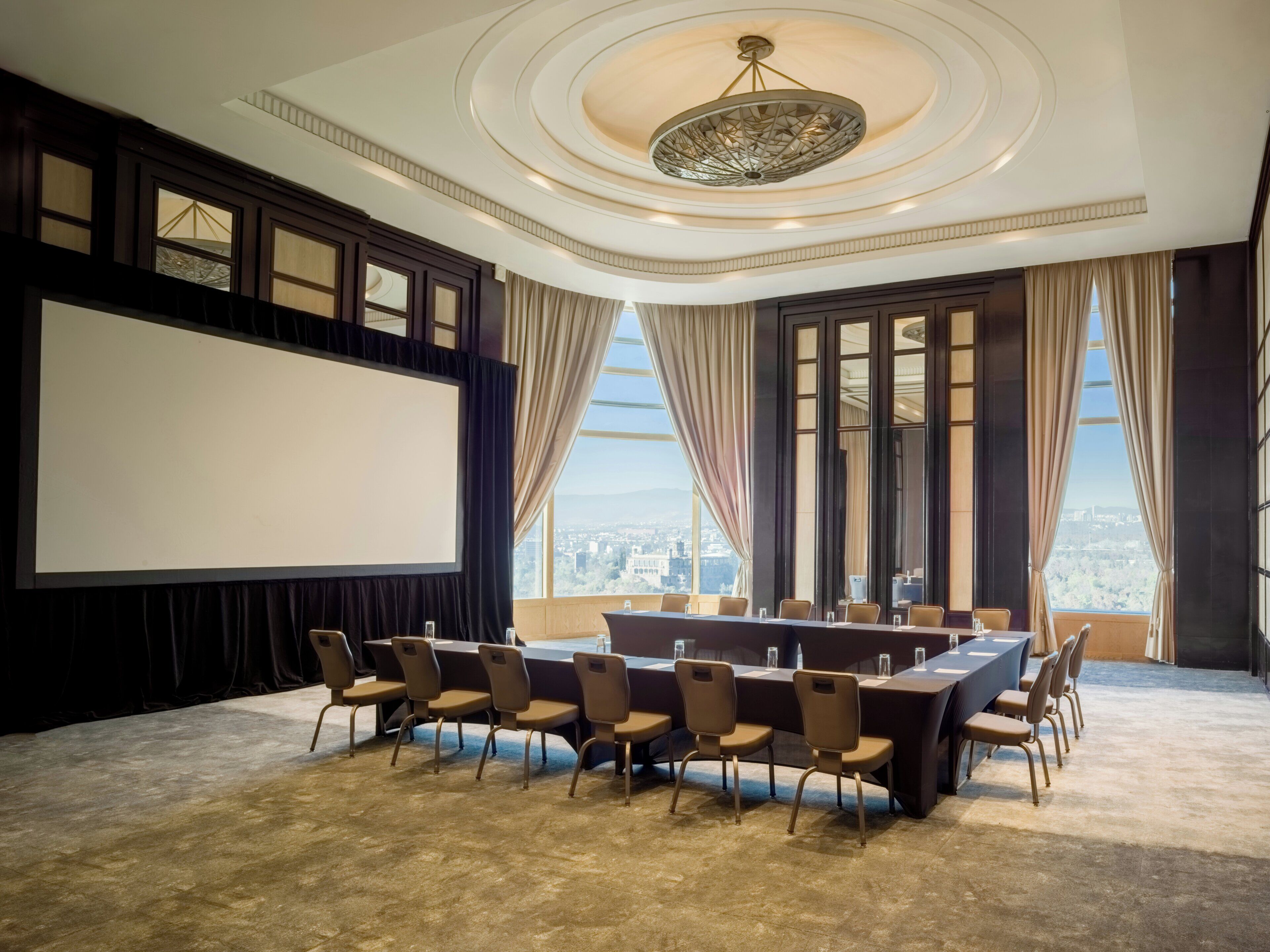 A conference room with a large table, chairs, a projector screen, and large windows with a city view.