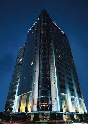 Een hoog, modern hotel met een opvallend verticaal ontwerp, grote ramen en een goed verlichte ingang.